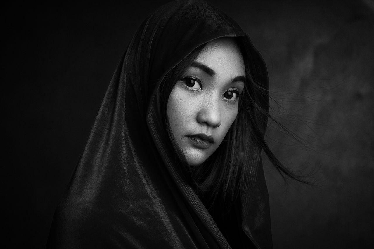 Home Elegant black and white portrait of a woman with a hooded cloak, exuding a moody and artistic tone.